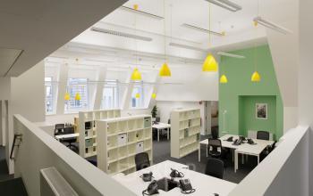 Modern office space rental at Fleischmarkt 1, in 1010 Vienna with bright yellow accents, desks, and telephones.