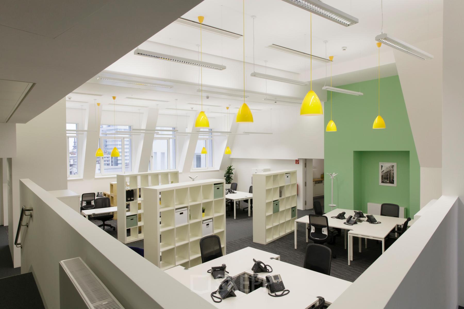 Modern office space rental at Fleischmarkt 1, in 1010 Vienna with bright yellow accents, desks, and telephones.