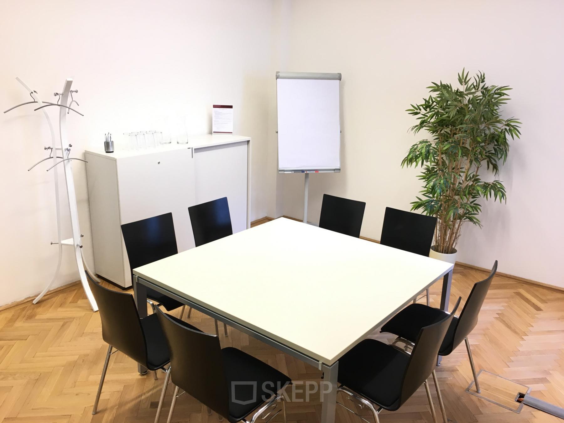 Well-lit conference room ideal for an office space rental at Graben 19, 1010 Vienna, featuring a large table, chairs, and a flipchart.