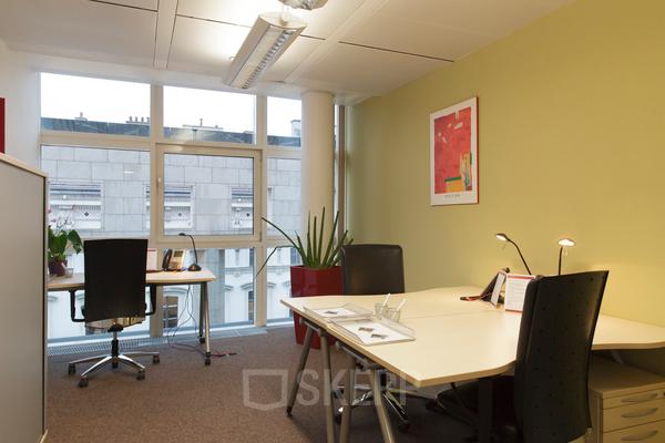 Well-lit office to rent at Kärntner Ring 5-7, 1010 Vienna featuring a desk, chairs, and a bright window with a city view.