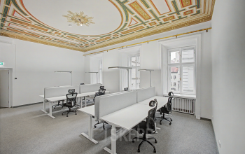 Lichtdurchflutetes Büro in 1010 Wien mit hohen Decken und ergonomischen Arbeitsplätzen unter einer kunstvollen Stuckdecke.