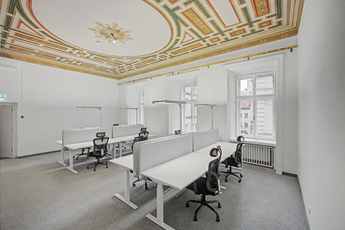 Lichtdurchflutetes Büro in 1010 Wien mit hohen Decken und ergonomischen Arbeitsplätzen unter einer kunstvollen Stuckdecke.