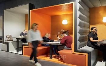 Modern office space rental at Nordbahnstraße 47, 1020 Vienna Leopoldstadt, featuring cozy workspaces with vibrant orange booths and focused professionals.