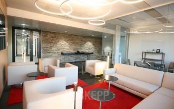 Moderne Lounge in einem Bürogebäude Am Belvedere 8, 1100 Wien, Favoriten, mit weißen Sofas und roten Teppichen.