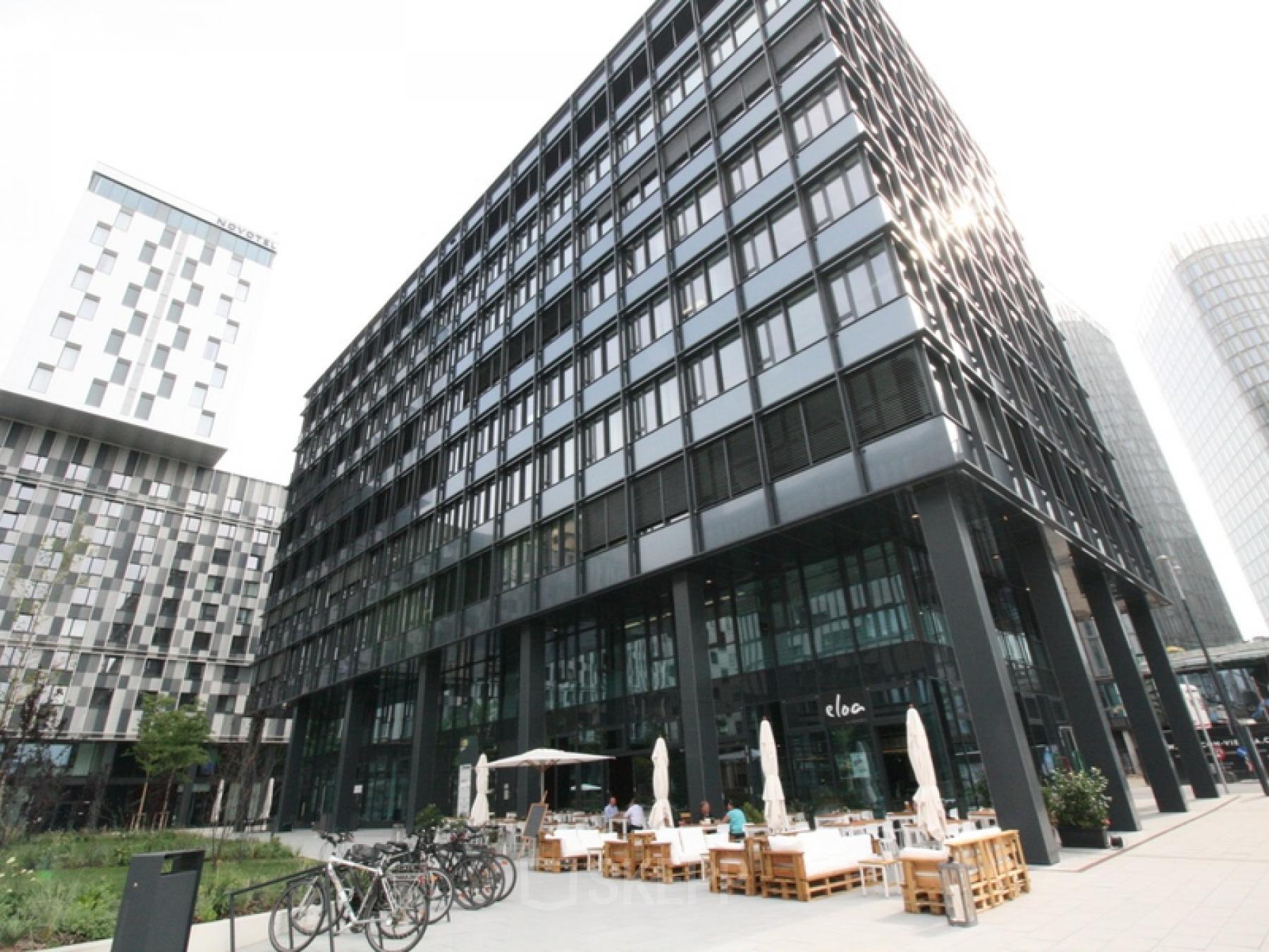 Modern office building at Am Belvedere 8, 1100 Vienna with outdoor seating area and bicycles parked in front.