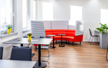 Modern office space rental at Wagenseilgasse 14, 1120 Vienna Meidling, featuring a vibrant red couch, stylish grey chairs, and a welcoming layout.