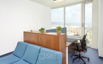 Bright furnished office space for rent at Floridsdorfer Hauptstraße 1, 1210 Vienna, featuring a desk, chair, plants, and a city view.