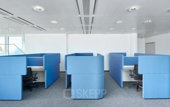 Modern office space rental at Floridsdorfer Hauptstraße 1 in 1210 Vienna, featuring individual blue cubicles with chairs, white desks, and ample natural light.