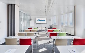 Spacious and modern conference room at Floridsdorfer Hauptstraße 1 in 1210 Vienna, featuring rows of tables and chairs, a large screen, and abundant natural light. Ideal for office space rental.