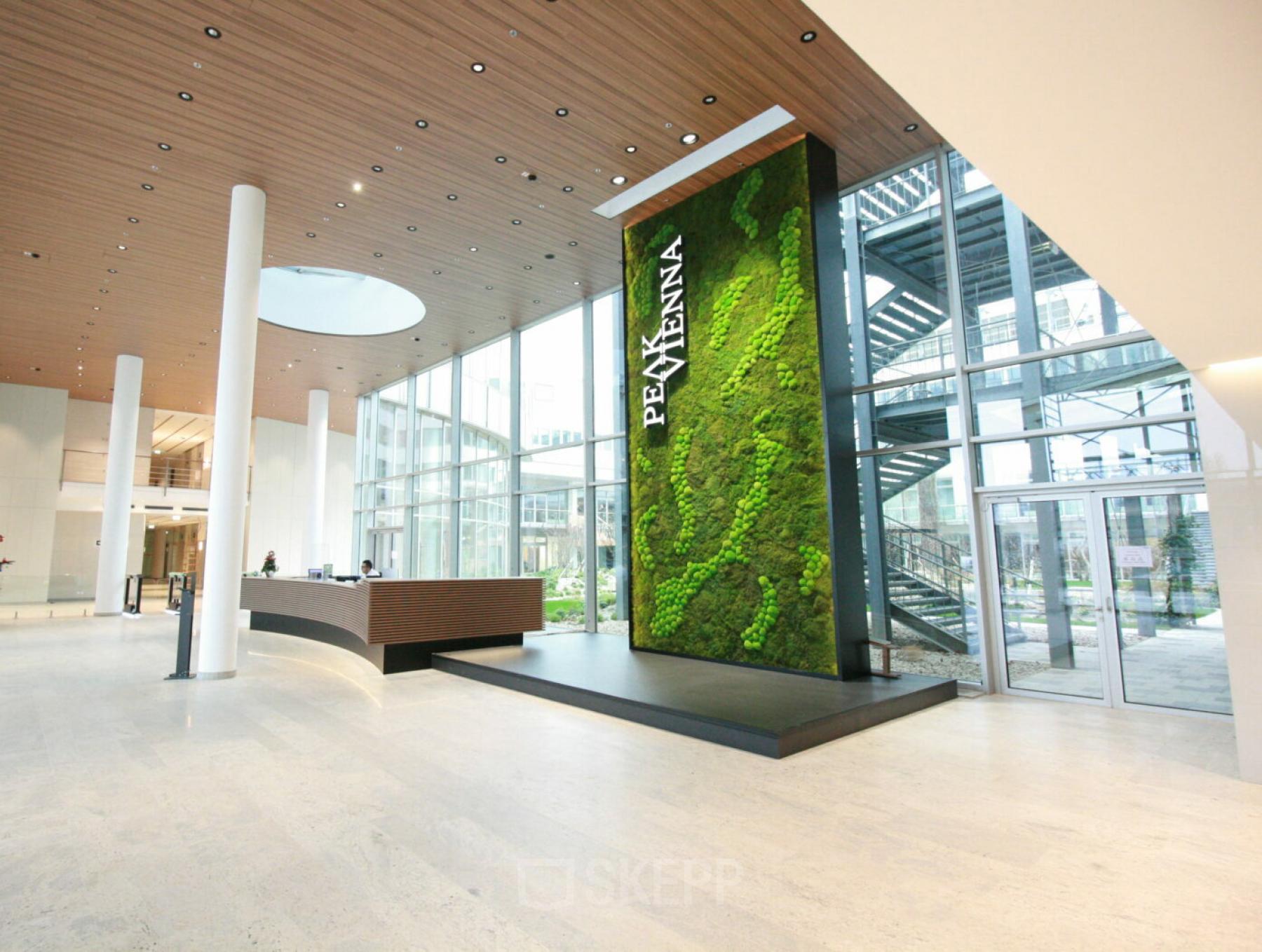 Modern reception area at Floridsdorfer Hauptstraße 1, 1210 Vienna, featuring a sleek desk and a large green vertical garden. Ideal office space rental in Floridsdorf.