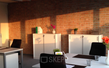 Well-lit office space rental at Kolbegasse 66, 1230 Vienna Liesing featuring white desks, brick walls, and modern decor.