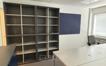 Innenansicht eines leeren Büroraums zur Miete in der Eitnergasse 13, 1230 Wien. Der Raum verfügt über große Regale, einen Schreibtisch und eine moderne Beleuchtung.