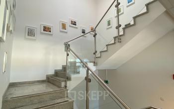 Modernes Treppenhaus in einem Büro in der Badener Straße 12, 2700 Wien Neustadt, mit eleganten Glasgeländern und Kunst an den Wänden.