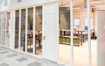 Modern office space rental at van Cleeffkade 15, Aalsmeer, featuring a workspace with desks, chairs, and office supplies seen through a glass wall.