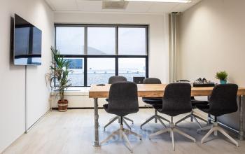 Modern office space rental at Van Cleeffkade 15 in Aalsmeer featuring a large table, chairs, potted plants, and a wall-mounted TV.