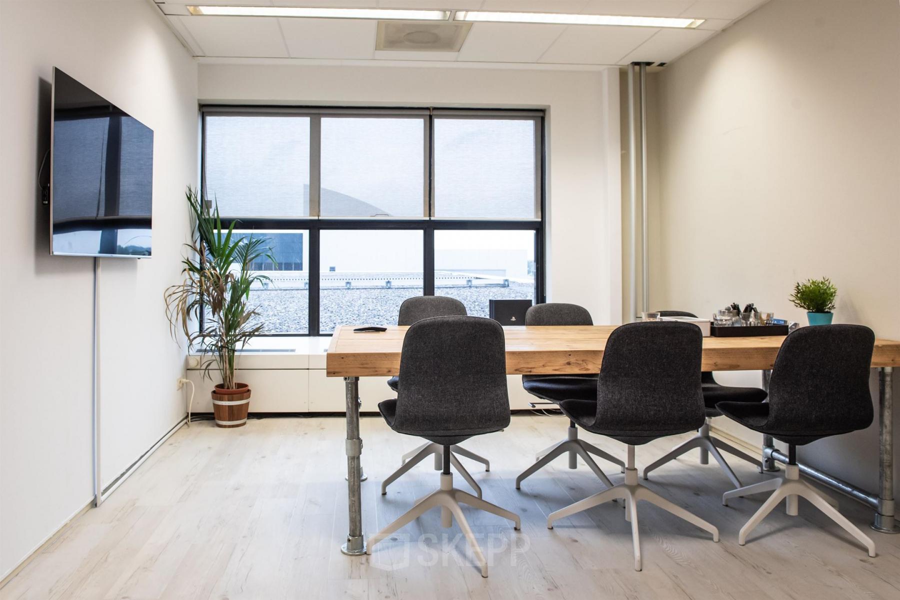 Modern office space rental at Van Cleeffkade 15 in Aalsmeer featuring a large table, chairs, potted plants, and a wall-mounted TV.