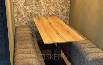 Office space available for rent at Hollandse Kade 38, Abcoude, features a stylish seating area with a wooden table, cushioned benches, and decorative lighting against a leaf-patterned wall.
