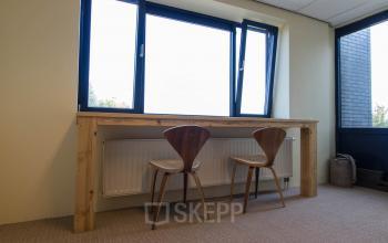 A well-lit office at Hollandse Kade 38, Abcoude, featuring a wooden desk with two modern chairs, ideal for those seeking office space rental. Ample natural light enhances the workspace environment.