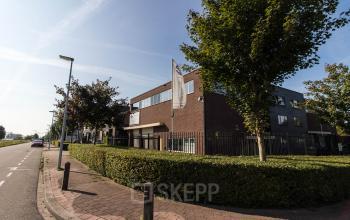 Exterior view of the office building at Hollandse Kade 38, Abcoude. The modern brick facade and lush greenery surround the perimeter, offering a welcoming glimpse for those interested in office space rental.