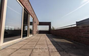 Spacious rooftop terrace with brick walls and large glass doors at an office space rental location on Hollandse Kade 38, Abcoude. Bright and open exterior perfect for breakout sessions.