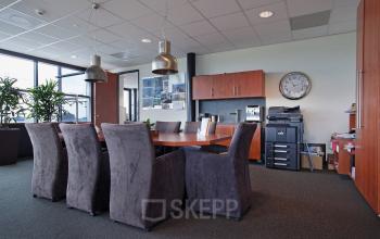 Office space rental at Twentepoort Oost 61, Almelo with a large meeting table, office chairs, plants, and a filing cabinet in the background.