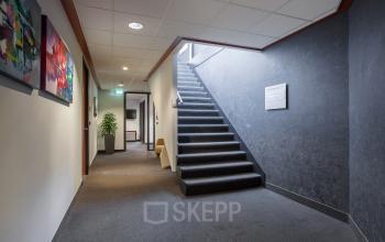 Interior view of office building located at Twentepoort Oost 61, Almelo, featuring a carpeted hallway with stairway and modern artwork on the walls. Ideal for office space rental.