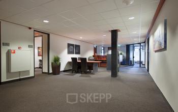 Modern office space with clean design at Twentepoort Oost 61, Almelo, featuring carpeted floors, a desk with chairs, and artworks on the wall for office space rental.