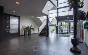 Modern entrance area in office building at Twentepoort Oost 61, Almelo, featuring large windows, a staircase, and potted plants. Ideal for office space rental.