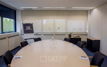 Meeting room at Markerkant 1310, Almere Stad, with a large round table and chairs, flip chart, and windows offering natural light.