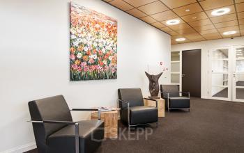 Stylish, furnished office space with modern chairs, a floral painting, and wooden side tables, perfect for rent at Leidse Schouw 2, Alphen aan den Rijn.