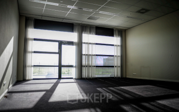 Bright office space with large windows at Leidse Schouw 2 in Alphen aan den Rijn, available for rent, featuring natural light and carpeted flooring.