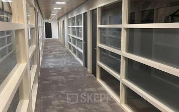 Long hallway with carpeted floor and glass partition walls in an office space for rent at Leidse Schouw 2, Alphen aan den Rijn.