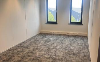 Empty office space with carpet flooring and two windows at Leidse Schouw 2 for rent in Alphen aan den Rijn.