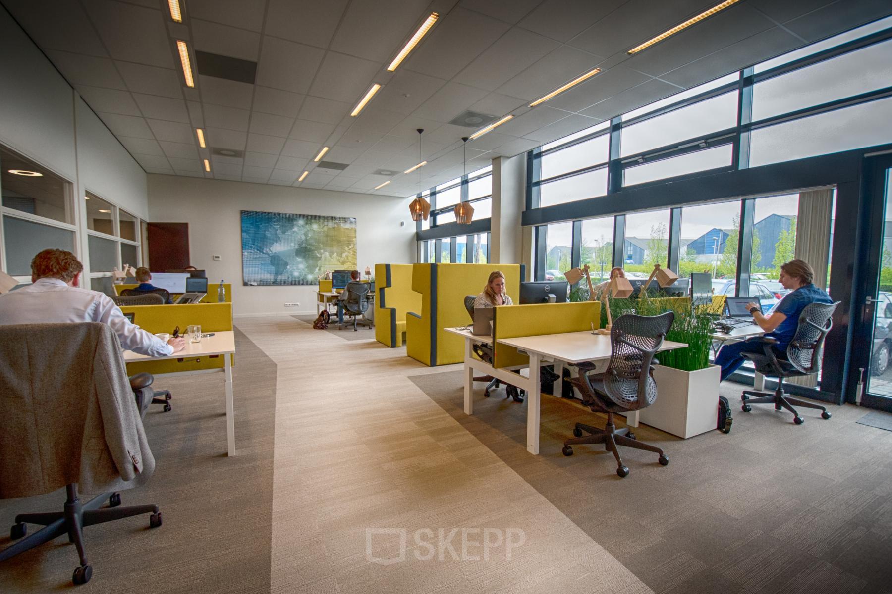 Modern office space with large windows, divided workstations, and professionals engaged in various business tasks, ideal for rent office space.