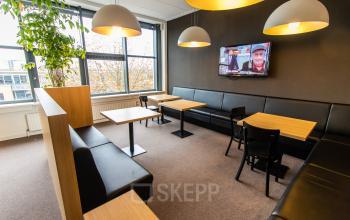 A cozy, furnished office lounge at Europalaan 16, Alphen aan den Rijn, featuring modern lighting, seating, and a wall-mounted TV—ideal for office space rental.