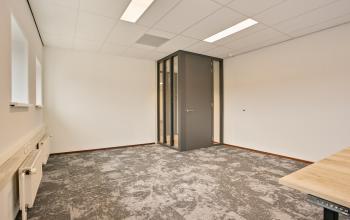 Modern office space at Astronaut 28, Amersfoort Calveen, featuring sleek gray carpet and a glass-walled private area, perfect for office space rental.