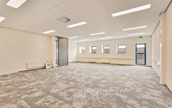 Spacious office interior at Astronaut 28, Amersfoort Calveen, showcasing a neutral carpeted floor and modern lighting, ideal for office space rental. Natural light filters through multiple windows.