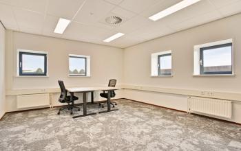 Bright office space with carpeted floors and two desks, located at Astronaut 28, Amersfoort Calveen. Ideal for office space rental with ample natural light through multiple windows.