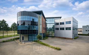 Modern office building located at Maanlander 43, Amersfoort Calveen, available for rent. Features a distinctive glass façade with ample parking space.