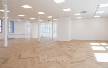 Spacious open office area at Maanlander 43, Amersfoort Calveen, featuring natural light and herringbone wooden flooring, ideal for office space rental.