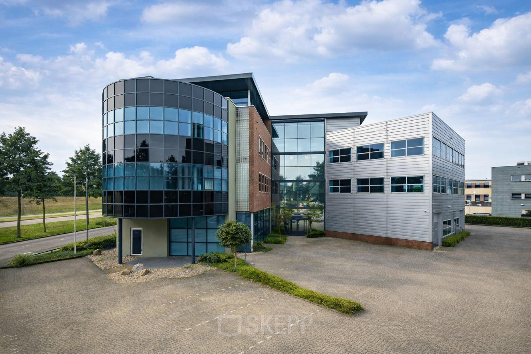 Modern office building located at Maanlander 43, Amersfoort Calveen, available for rent. Features a distinctive glass façade with ample parking space.