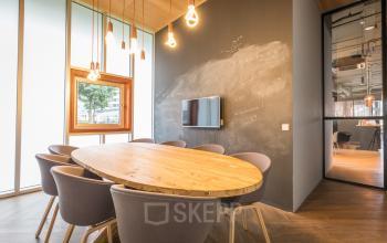 Modern conference room at Maanlander 47, Amersfoort Calveen, suitable for office space rental, featuring a wooden table, chairs, chalkboard wall, and pendant lights.