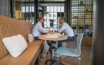 Two people having a business discussion in a stylish furnished office to rent at Maanlander 47, Amersfoort Calveen, featuring modern decor ideal for office space rental.