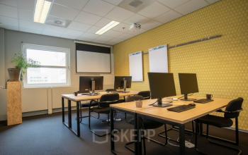 Modern office space with desks and computers at Stationsplein 49, Amersfoort Centraal Station, available for office space rental. The room features a projector and natural light.
