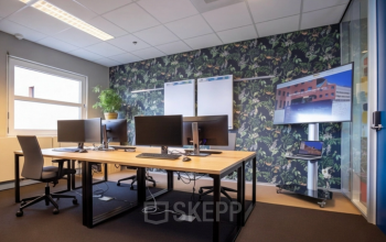 Stylish office space featuring multiple computer workstations, a large screen, and a plant, ideal for office space rental at Stationsplein 49, Amersfoort Centraal Station.