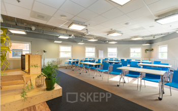 Bright and functional office space available for rent at Stationsplein 49, Amersfoort Centraal Station. Featuring rows of blue chairs and white desks, perfect for business activities.