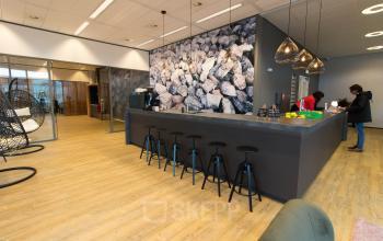 Modern office interior at Smallepad 32 in Amersfoort Centraal Station, featuring a sleek bar area, stools, and contemporary lighting. Two people interact at the counter, ideal for office space rental.