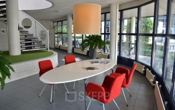 A modern office space rental at Algolweg 9-11, Amersfoort De Hoef, featuring a stylish meeting area with red chairs and a white oval table.