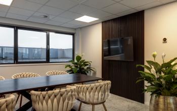 Contemporary conference room at Vanadiumweg 11, Amersfoort Isselt, featuring a sleek table, comfortable chairs, wall-mounted screen, and natural light streaming through large windows. Ideal for office space rental.