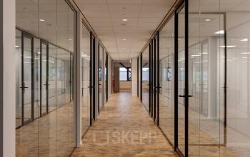 Corridor in Vanadiumweg 11, Amersfoort Isselt, featuring glass-walled rooms suited for office space rental, with natural light and parquet flooring offering a modern and professional atmosphere.